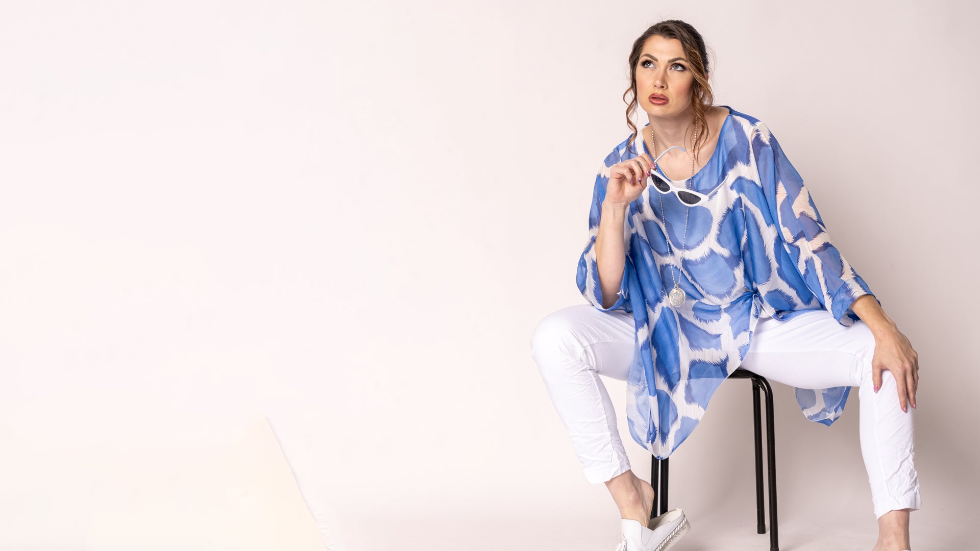 Woman wearing a blue and white patterned top sitting on a chair against a plain background